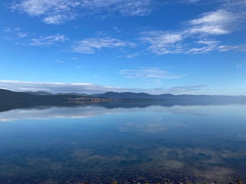 Peaceful Presence, view of a very still lake with mountains in the background. Blue Sky.